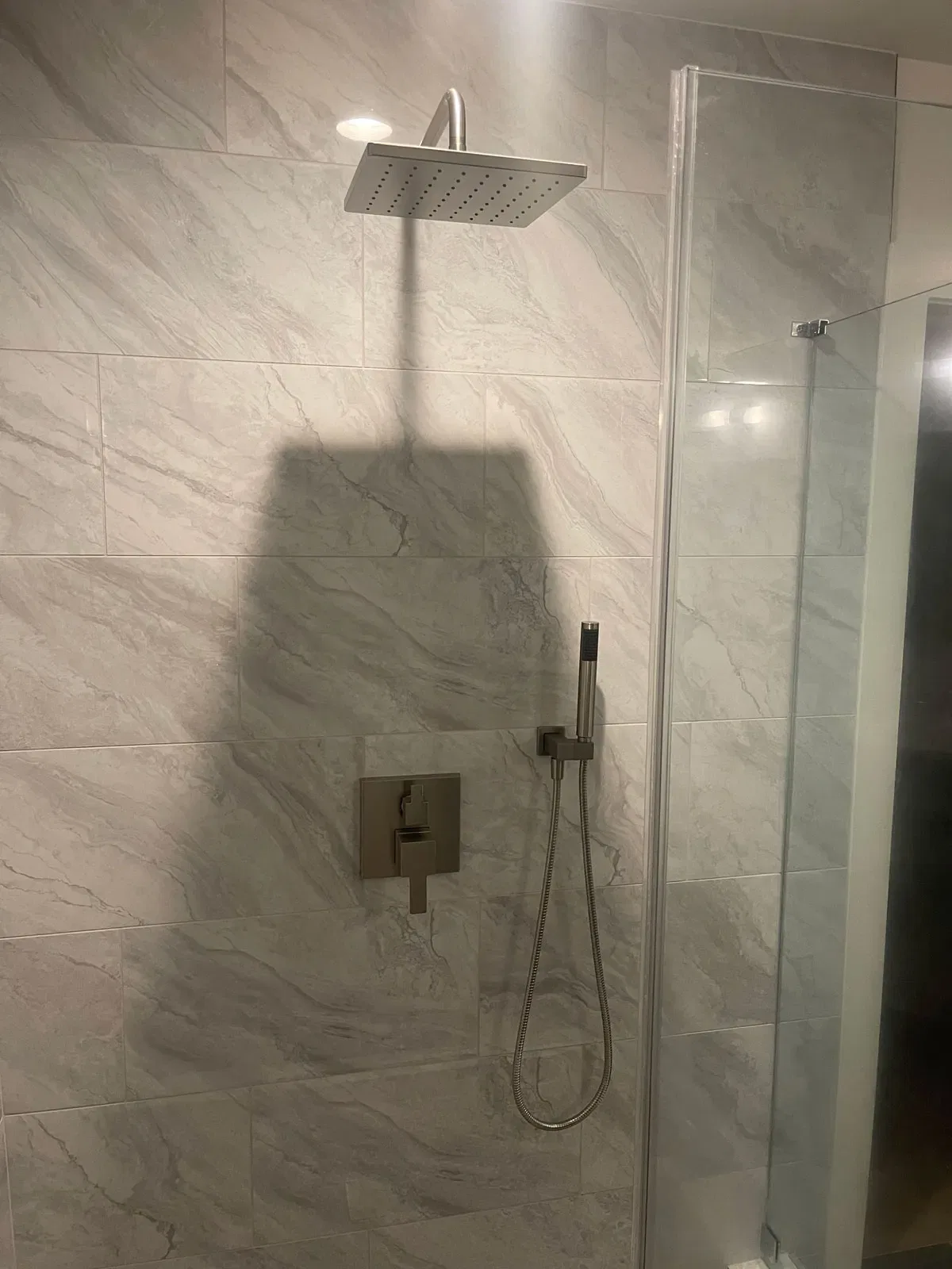 Modern shower head in a tiled bathroom with glass door